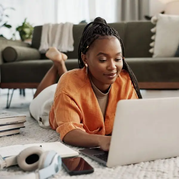 femme qui regarde son ordinateur sur son tapis dans son salon