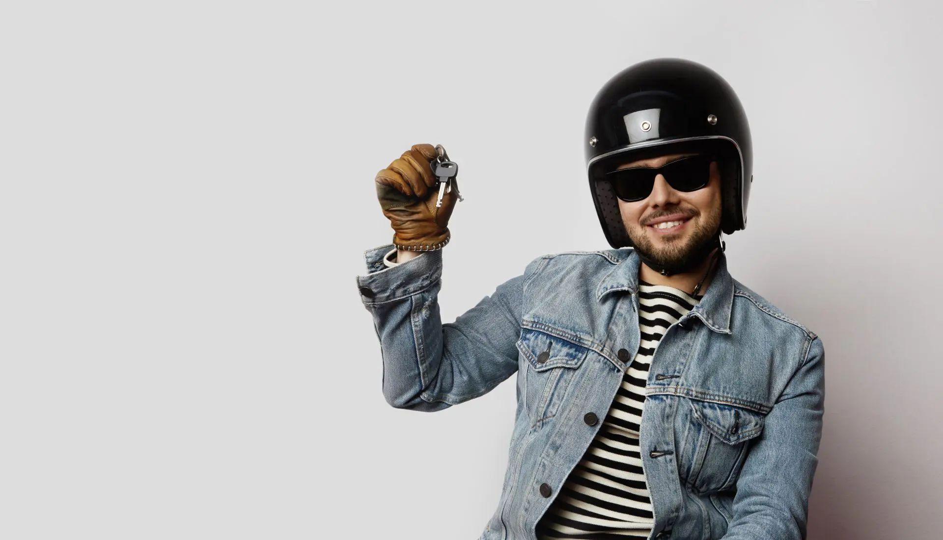 Jeune motard dans une veste en Jean bleu faisant semblant de conduire une moto et tenant une clé de moto