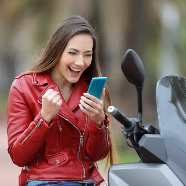 Femme qui regarde son téléphone en souriant sur son scooter