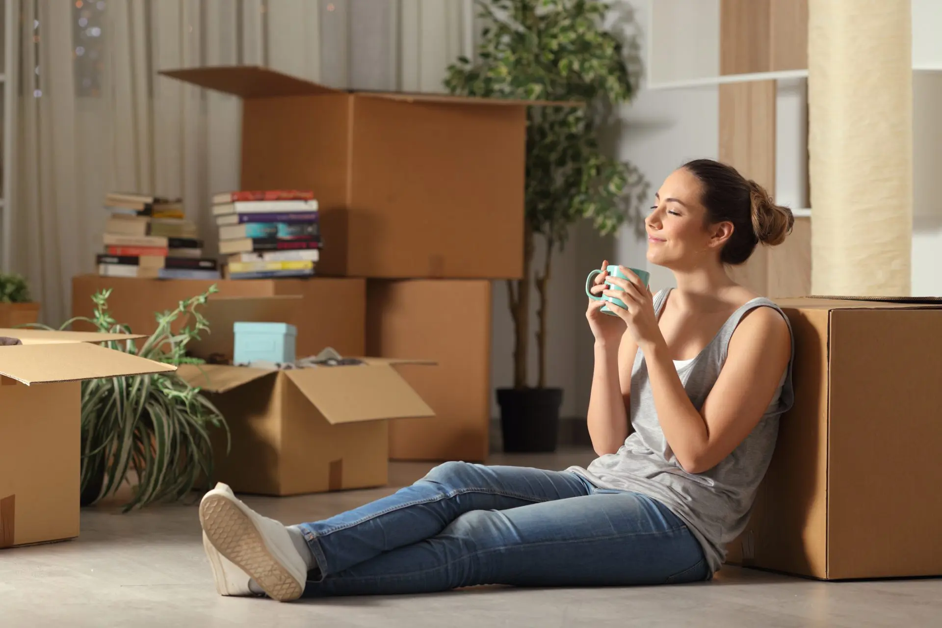 Femme avec une tasse, entourée de ses cartons dans maisons avec un air heureux