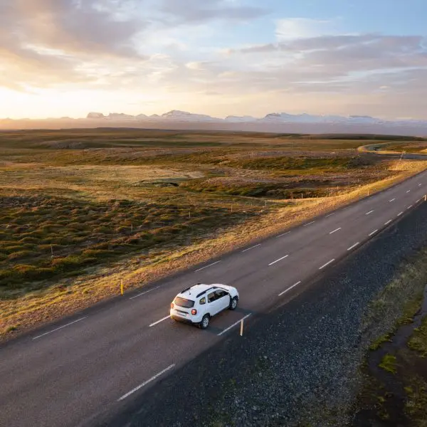 voiture sur la route entourée de champs avec un coucher de soleil sur le côté.