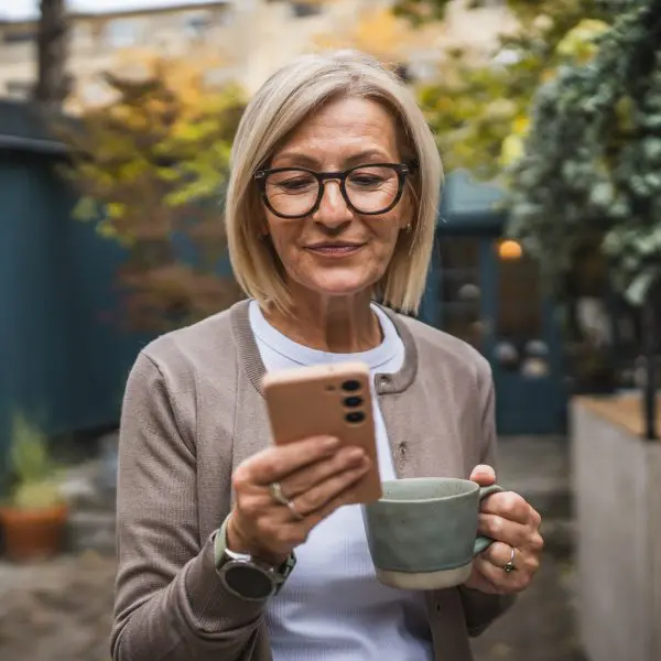 Femme âgée joyeuse faisant une pause, en prenant un café et en utilisant un téléphone portable