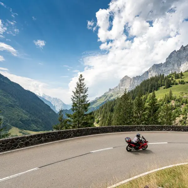 Une moto roule sur une route sinueuse dans les montagnes des Alpes suisses