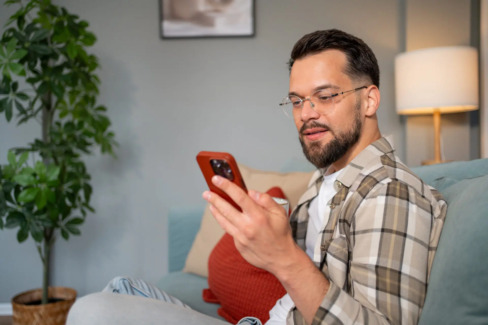 Jeune homme se relaxant sur le canapé à l’aide d’un smartphone et buvant du café 