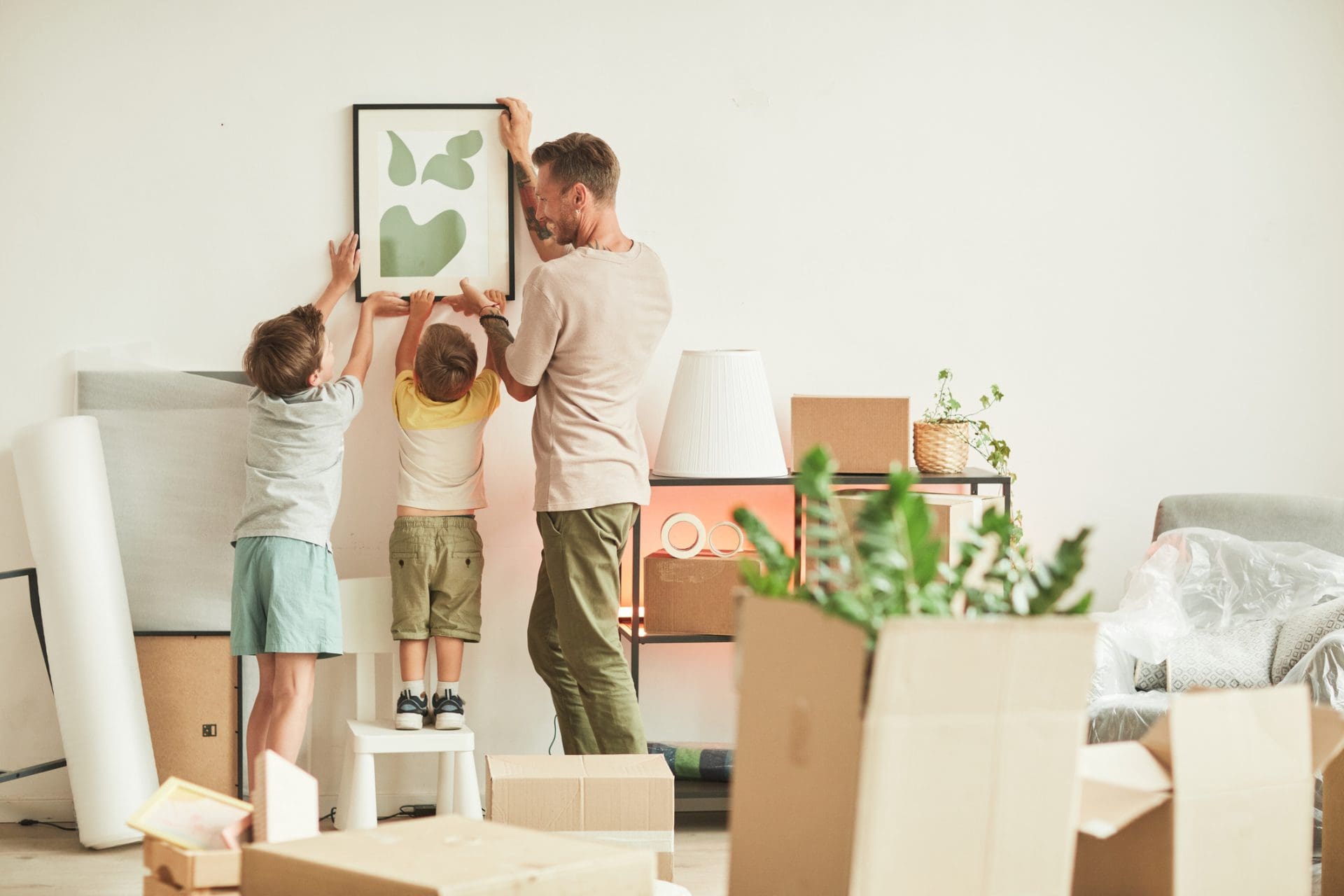 Un adulte qui installe un tableau avec ses deux enfants dans une nouvelle maison