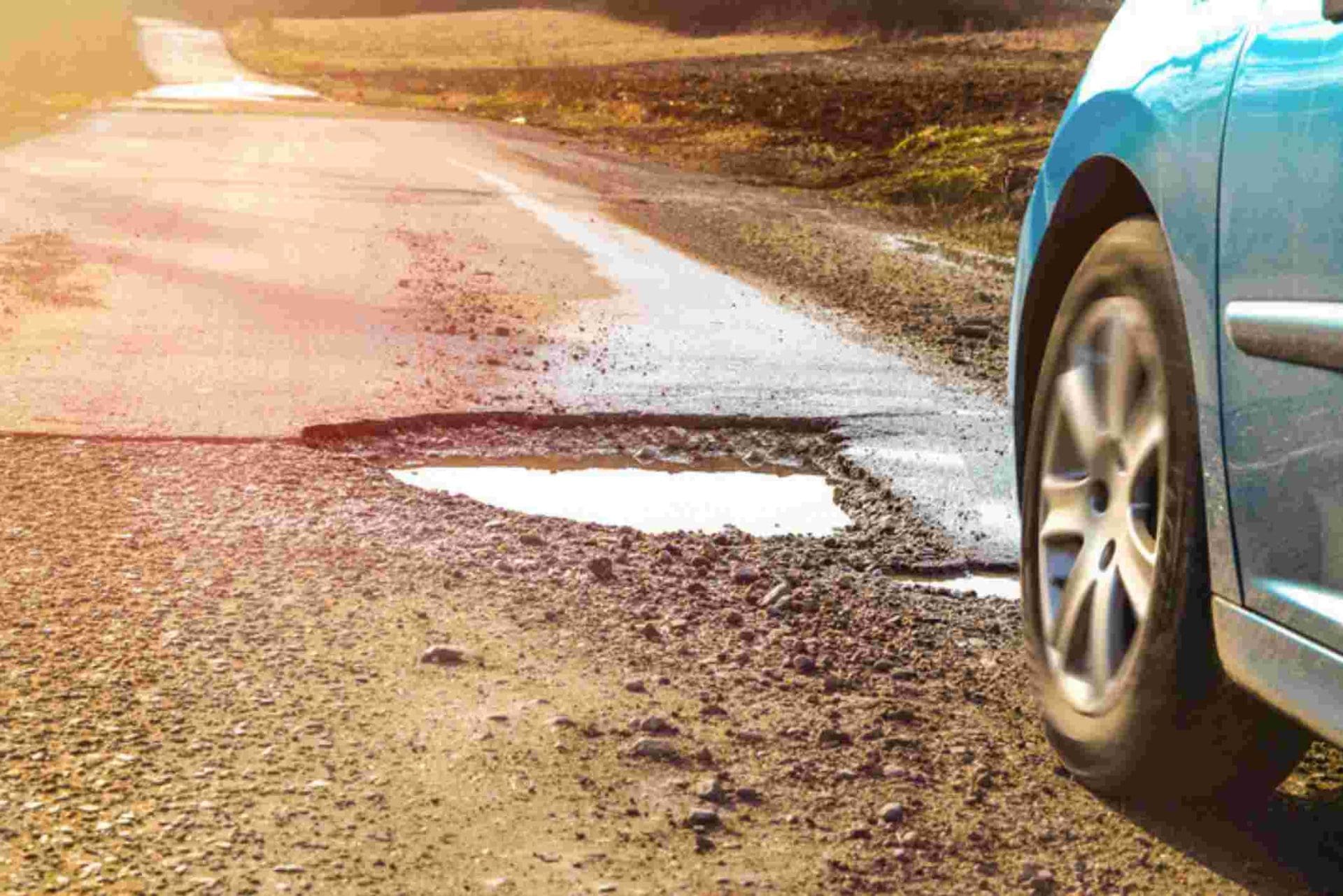 pneu de voiture à côté d'un nid de poule sur une route abîmée