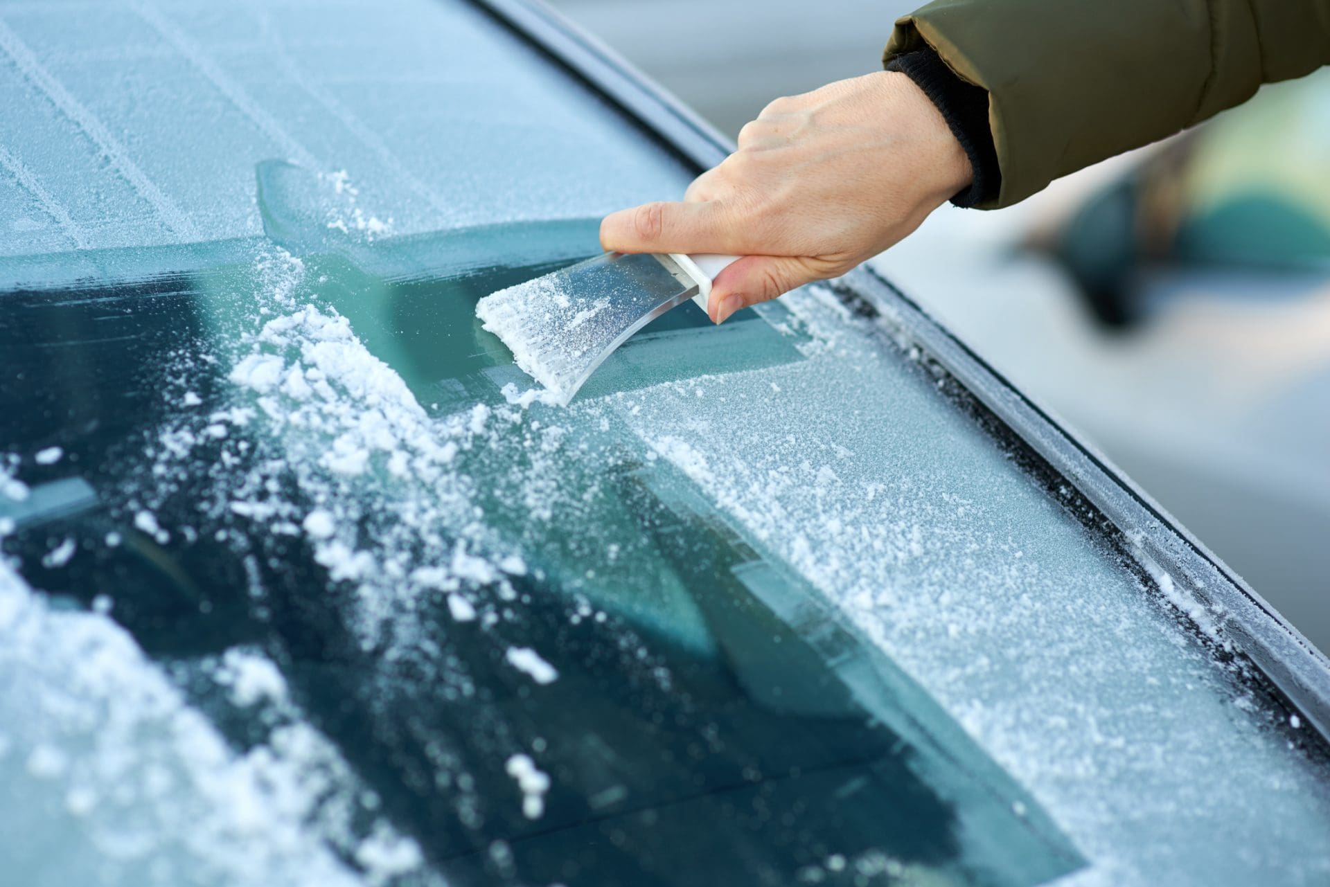 main qui déneige sa voiture avec un grattoir