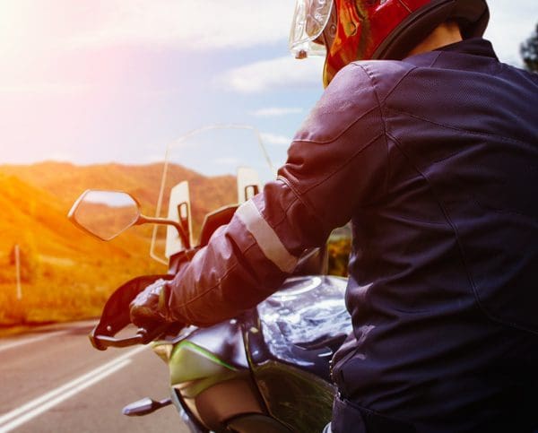 Vue de l'arrière d'un motard sur sa moto restant sur le bord de la route et regardant à l'horizon avec des montagnes