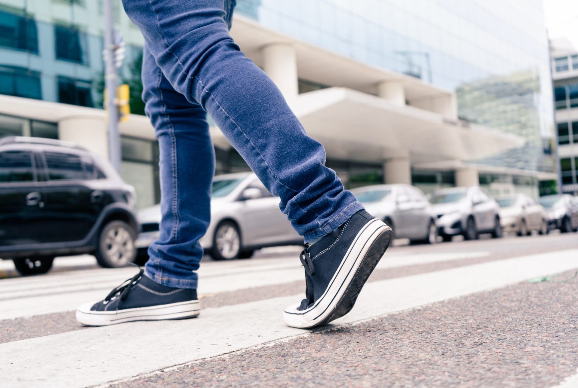 Plan rapproché des pieds d’un homme dans des baskets noires traversant une rue sur le chemin zébré ou piétonnier.