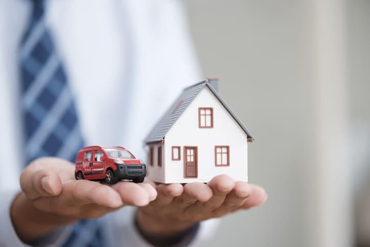 Agent immobilier détenant des modèles de maisons et de voitures symbolisant l’assurance des biens et des véhicules