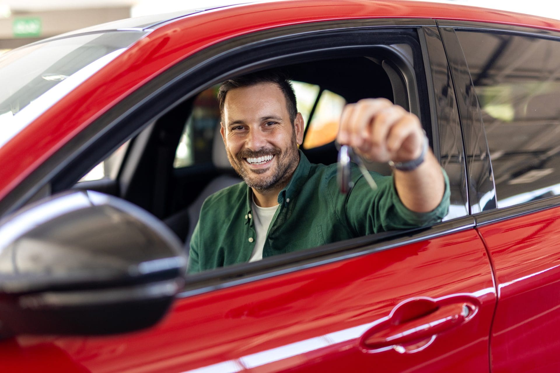 Homme tenant des clés dans sa nouvelle voiture, souriant à la caméra. 