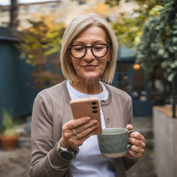 Femme âgée joyeuse faisant une pause, en prenant un café et en utilisant un téléphone portable