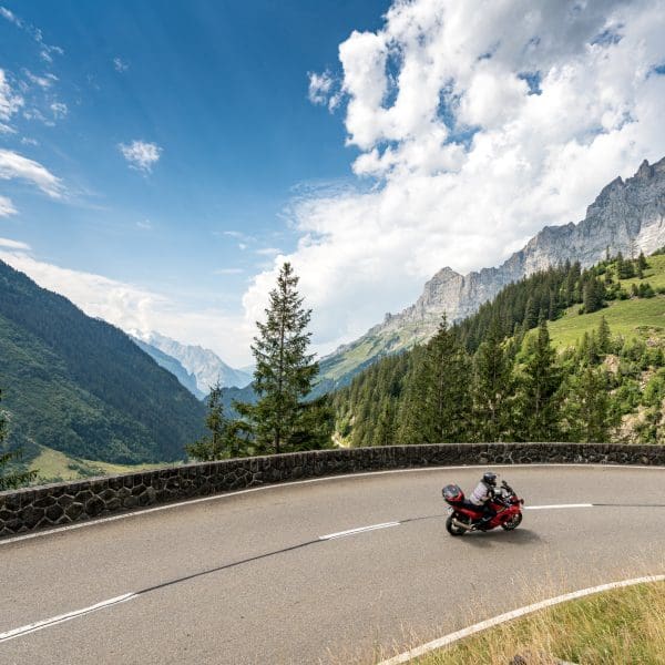 Une moto roule sur une route sinueuse dans les montagnes des Alpes suisses
