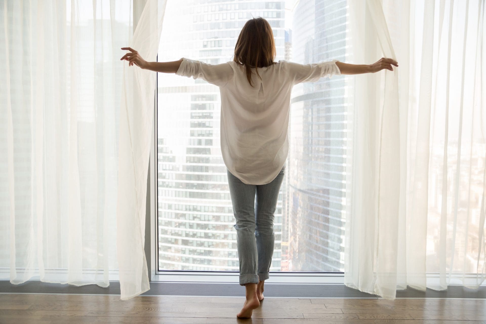Femme debout regarde par la fenêtre ouvrir les rideaux, vue arrière