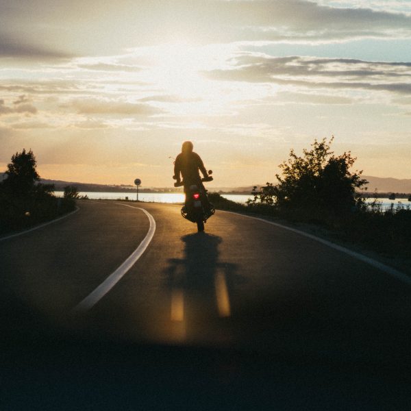 Personne conduisant une moto sur une route étroite pendant l’heure d’or